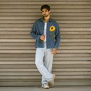 Full-length look of man wearing blue denim shaket with embroidered sunflower and light wash jeans