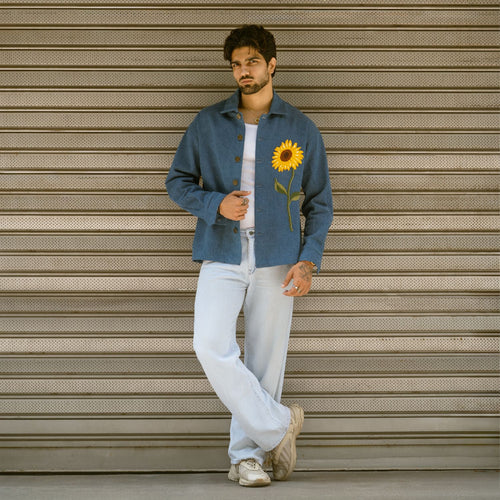Full-length look of man wearing blue denim shaket with embroidered sunflower and light wash jeans