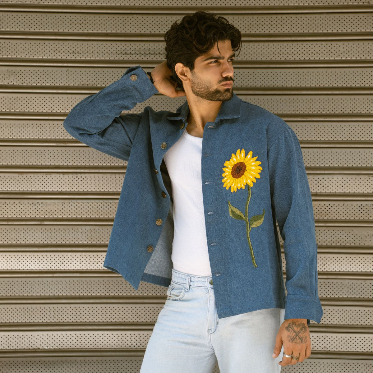 Man posing in open blue denim shaket showing embroidered French knot sunflower on the front